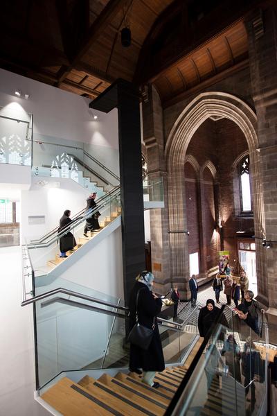 Image of All Soul's Church interior, showing the modern staircase with people walking up the stairs, agains the historic entrance.