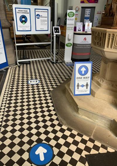 Interior view of the entrance of All Souls', with prominent signage informing visitors of the one way system, need to wear a face covering unless exempt and hand sanitising station.