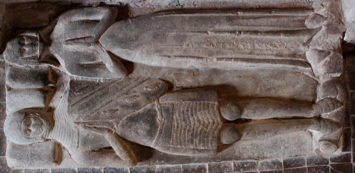 Effigies of an armoured knight and a lady laying beside each other. The knight has a shield on their left arm carved with the arms of the local family of de la Bere.