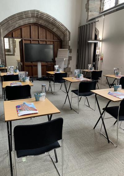 Single person desks, spaced out to enable social distancing inside one of the meeting rooms All Souls' Bolton. Each desk has a water bottle and cup, writing utensils and a delegate information pack.